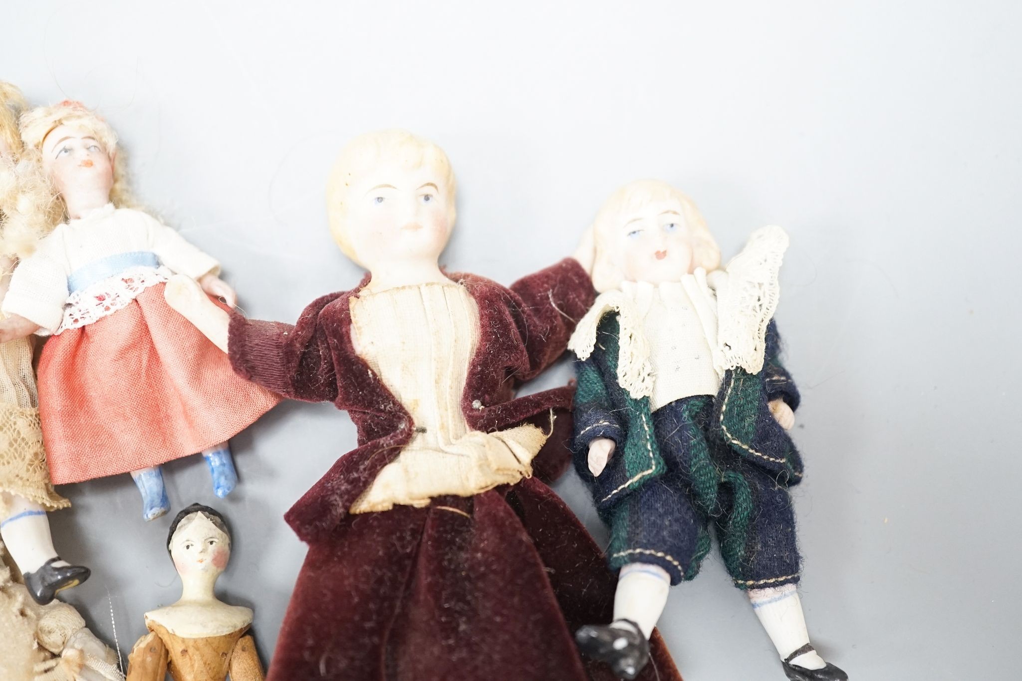 A collection of miniature bisque dolls and another larger doll in a wooden cradle, 11 dolls in total., Cradle 23.5 cms long.